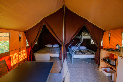 Innenansicht eines Ponza Safari-Zeltes bei Onlycamp Camping Les Thézières mit Betten, Tisch und Küche.