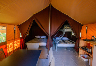 Innenansicht eines Ponza Safari-Zeltes bei Onlycamp Camping Les Thézières mit Betten, Tisch und Küche.
