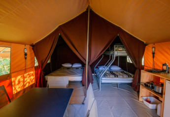 Interno della tenda safari Ponza a Onlycamp Camping Les Thézières con letti, tavolo da pranzo e cucina.