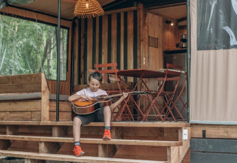 Bambino seduto sui gradini di una tenda safari chiamata Tiny house Galli, suona la chitarra fuori.