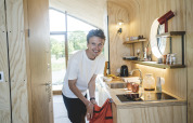 Homme souriant dans une cuisine de lodge moderne en bois clair, vue sur la nature par la fenêtre.