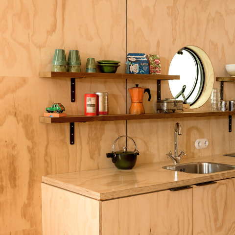 Gezellige lodge-keuken met houten wandbekleding, open planken, keukengerei en een rond raam.