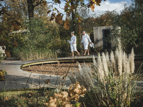 Twee mensen in badjas lopen bij een Wikkelhouse op Resort de Parel in Nederland, omgeven door herfstnatuur.