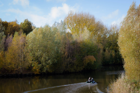 Deux personnes rament sur une petite barque sur une rivière calme, entourée d’arbres d’automne à Wikkelhouse.