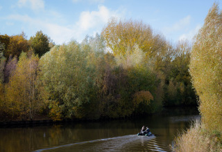 Twee mensen roeien in een bootje op een rustige rivier omringd door herfstbomen bij Wikkelhouse, de Parel.