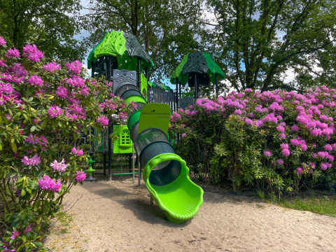 Parque infantil con tobogán verde entre flores rosadas en el Holiday park Latour, Brabante Septentrional, Países Bajos.