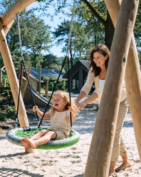 Eine Frau schaukelt ein lachendes Kind auf einem Spielplatz im Holiday Park Latour, Noord-Brabant, Niederlande.