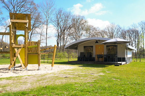 Villa tienda safari y área de juegos en Campsite de Witte Berg, Países Bajos, rodeada de naturaleza verde.