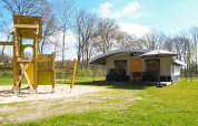 Safari tent villa and playground at Campsite de Witte Berg in the Netherlands, surrounded by grassy nature.
