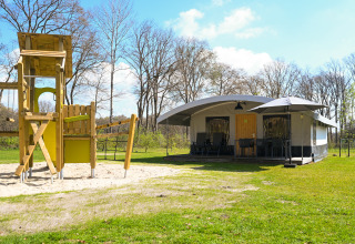 Safari tent villa and playground at Campsite de Witte Berg in the Netherlands, surrounded by grassy nature.