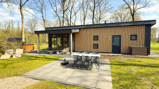 Modern wood cottage with outdoor terrace, dining table, chairs, and trees, taken on a bright sunny day.