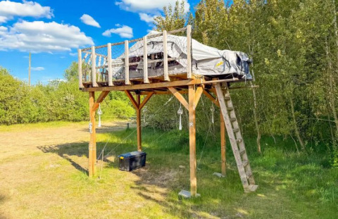 Verhoogde glampingtent op houten platform bij Dachzelt Dorf Sandstedt, omgeven door bomen en gras.