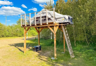Elevated glamping tent on a wooden platform at Dachzelt Dorf Sandstedt, surrounded by trees and grass.