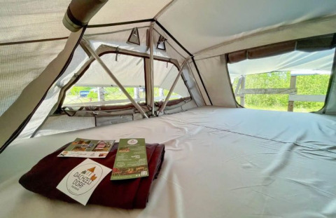 Vue intérieure d’une tente glamping au Dachzelt Dorf Sandstedt avec lit confortable et vue nature.