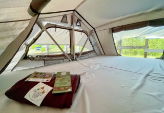 Interior de una tienda glamping en Dachzelt Dorf Sandstedt, con cama cómoda y vista a la naturaleza.