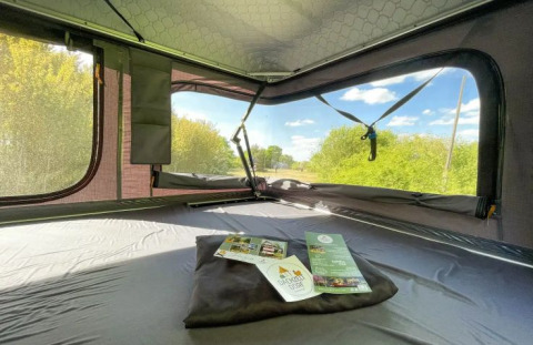 Innenansicht eines Dachzelts im Dachzelt Dorf Sandstedt, mit Ausblick auf sonnige Natur und Himmel.