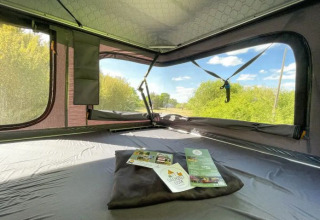 Binnenaanzicht van een daktent bij Dachzelt Dorf Sandstedt, met uitzicht op groen en blauwe lucht.