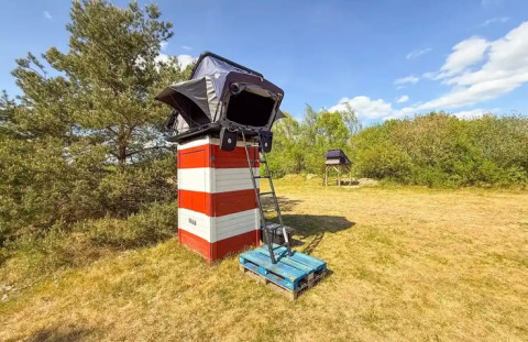 Glamping tent on an elevated platform at Dachzelt Dorf Sandstedt surrounded by grass and blue sky.