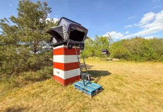 Glamping con tenda su piattaforma rialzata al Dachzelt Dorf Sandstedt, prato e cielo azzurro.