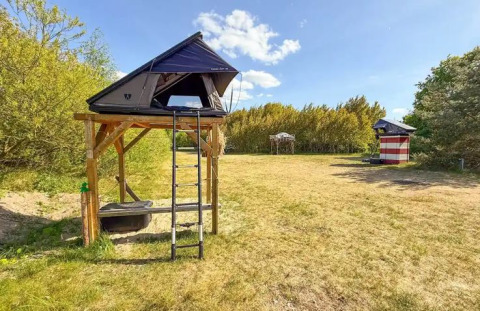 Glamping Dachzelt Dorf Sandstedt con tenda rialzata, scala e ampio prato circondato da alberi.