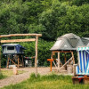 Glamping accommodation at Dachzelt Dorf Freilingen featuring raised tents, a beach chair, and lush greenery.