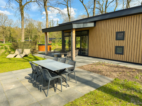 Terrasse extérieure avec table à manger, chaises longues et jacuzzi à Wood Cottage, Camping de Witte Berg, Pays-Bas.