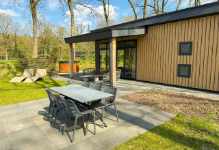 Outdoor patio with dining table, lounge chairs, and hot tub at Wood Cottage, Campsite de Witte Berg, Netherlands.