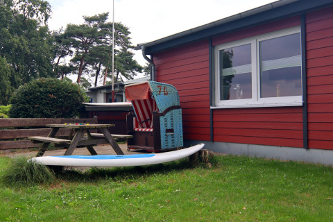 Buitenruimte bij lodge 'Am Strand' in Duitsland met picknickbank, strandstoel en surfplank op het gras.