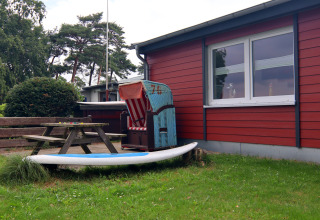 Buitenruimte bij lodge 'Am Strand' in Duitsland met picknickbank, strandstoel en surfplank op het gras.