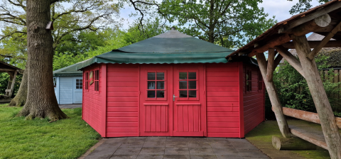 Bright red wooden writer’s cabin with green roof, nestled among trees and greenery in a natural setting.