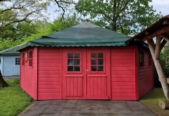 Cabaña de escritor roja con techo verde, rodeada de árboles y vegetación en un entorno natural.