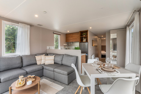Zona giorno luminosa nel chalet Vakantiehuis Deluxe con divano grigio, tavolo da pranzo e cucina moderna.