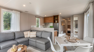 Zona giorno luminosa nel chalet Vakantiehuis Deluxe con divano grigio, tavolo da pranzo e cucina moderna.