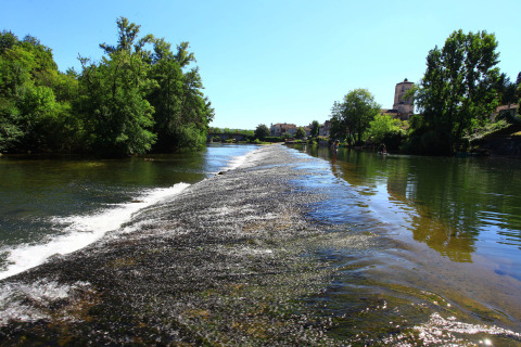 Vista sul fiume al campeggio Le Périgord in Nouvelle-Aquitaine, Francia, con alberi e villaggio sullo sfondo.