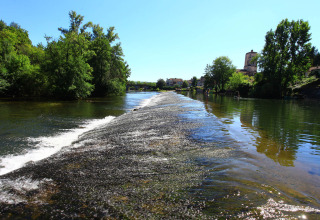 Vista sul fiume al campeggio Le Périgord in Nouvelle-Aquitaine, Francia, con alberi e villaggio sullo sfondo.