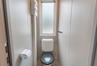Bagno moderno con sedile grigio, finestra smerigliata in Vakantiehuis Deluxe al Camping Papillon in Belgio.
