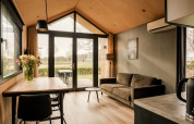 Modern tiny house living room with sofa, dining table, flowers and garden view in the Netherlands.