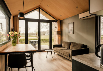Moderne tiny house stue med sofa, spisebord, blomster og udsigt mod haven i Nederlandene.