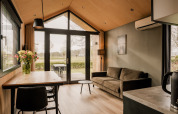 Modernes Tiny House Wohnzimmer mit Sofa, Esstisch, Blumen und Blick auf den Garten in den Niederlanden.
