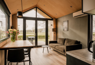 Moderne tiny house stue med sofa, spisebord, blomster og udsigt mod haven i Nederlandene.