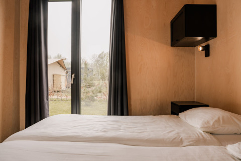 Soveværelse i et tiny house på Holiday park Eigen Wijze i Holland med dobbeltseng og udsigt udendørs.