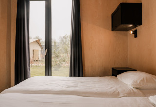 Soveværelse i et tiny house på Holiday park Eigen Wijze i Holland med dobbeltseng og udsigt udendørs.