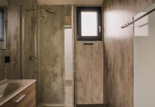 Baño moderno con ducha, lavabo y ventana pequeña en una tiny house del Holiday park Eigen Wijze, Países Bajos.