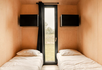 Tiny house bedroom with two single beds and window view at Holiday park Eigen Wijze, Netherlands.