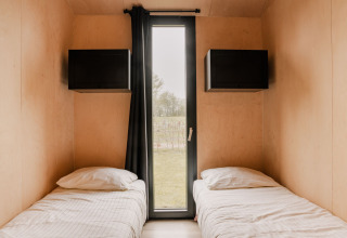 Dormitorio de tiny house con dos camas individuales y ventana en Holiday park Eigen Wijze, Países Bajos.