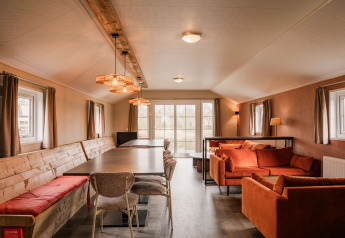 Innenraum der Group Lodge im Holiday Park Eigen Wijze mit langen Tischen, Sofas und Fenstern.