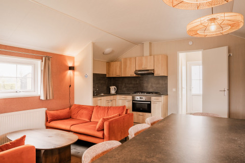 Helles Lodge-Interieur mit moderner Küche und orangefarbenem Sofa im Ferienpark Eigen Wijze, Niederlande.