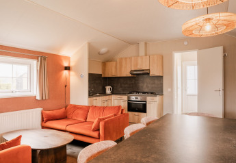 Helles Lodge-Interieur mit moderner Küche und orangefarbenem Sofa im Ferienpark Eigen Wijze, Niederlande.