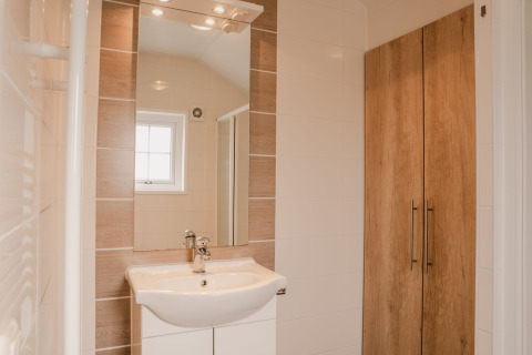 Baño moderno en Group lodge, Holiday park Eigen Wijze, con lavabo, espejo y armario de madera.
