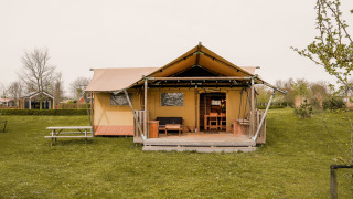 Tienda de glamping tipo safari con porche de madera y mesa de picnic en césped, rodeada de naturaleza.